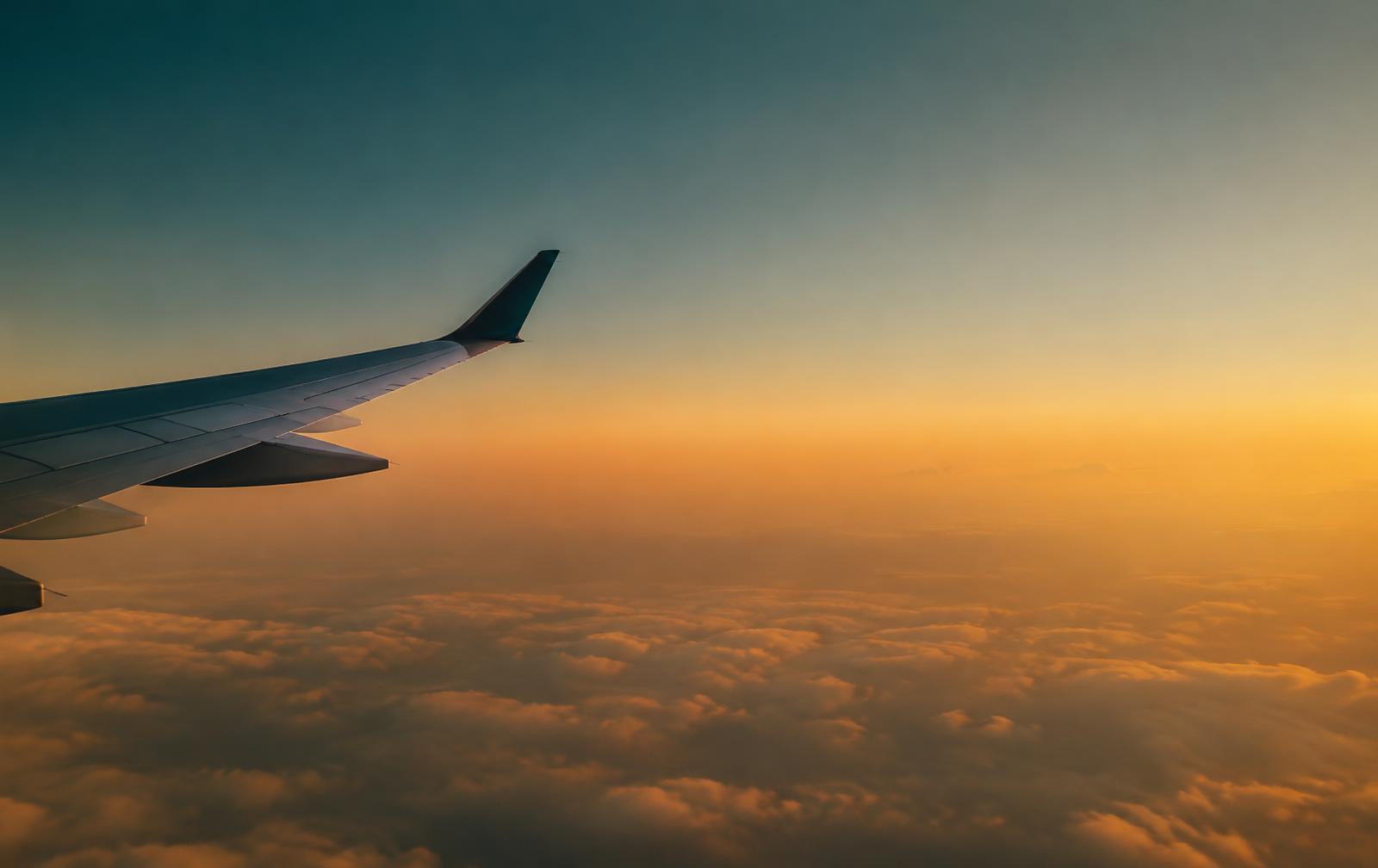 Airplane wing above clouds at sunset